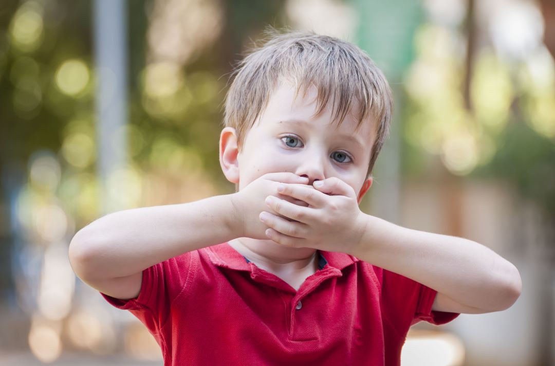 Little boy covering his own mouth with his hands