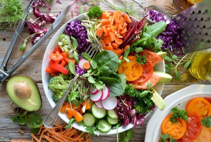 Fresh salad in a bowl surrounded by kitchen utensils and stray vegetables