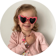 Our member Imogen smiling wearing heart sunglasses and showing her pink MedicAlert Kids Silicone Bracelet: MedicAlert for Coeliac Disease