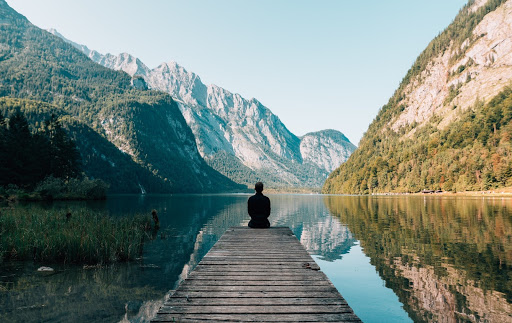 Person sat on the end of a pontoon infront of a lake and a mountain range