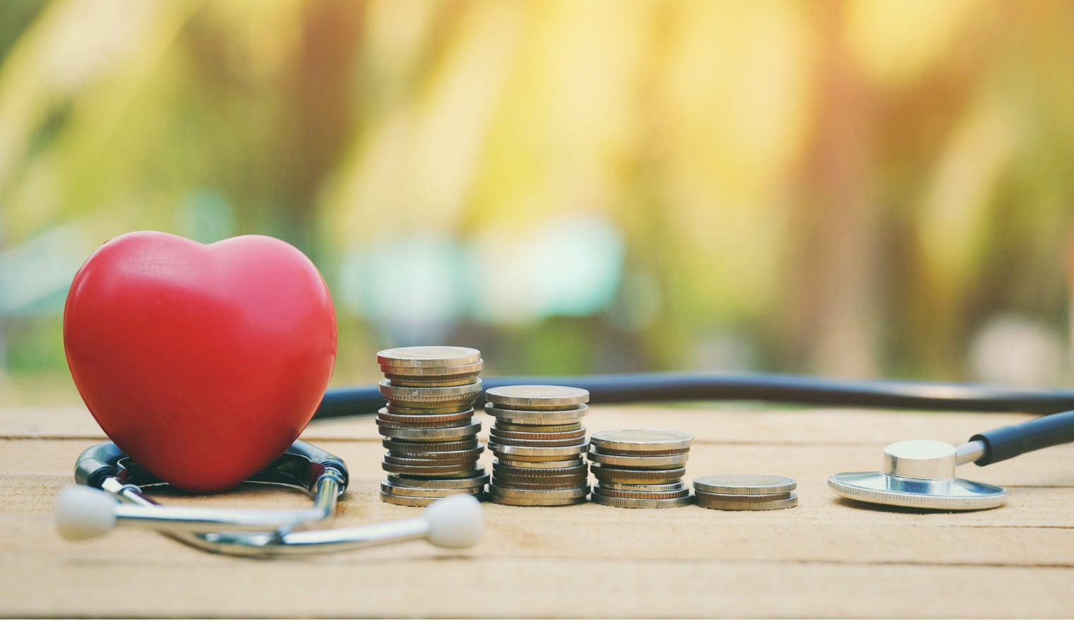 Red glass heart on top of a stethoscope next to stacks of coins