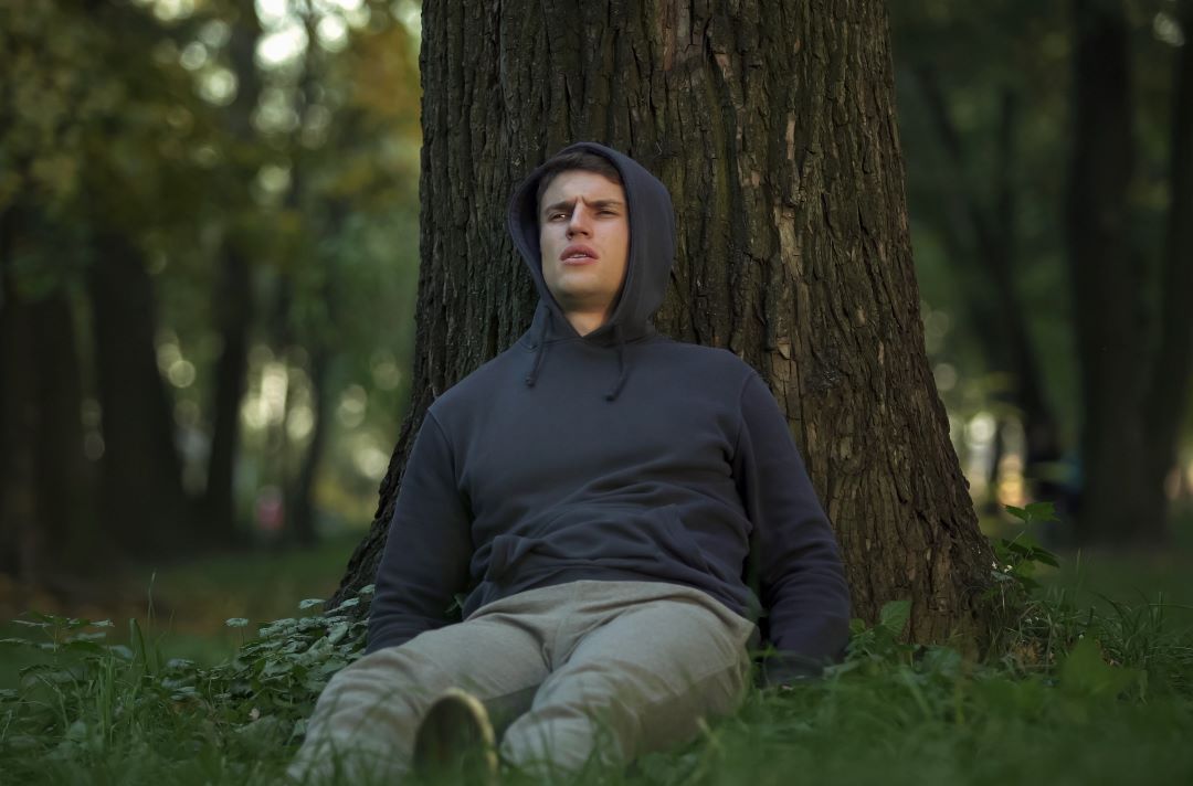 A sick man in the forest laying against a tree