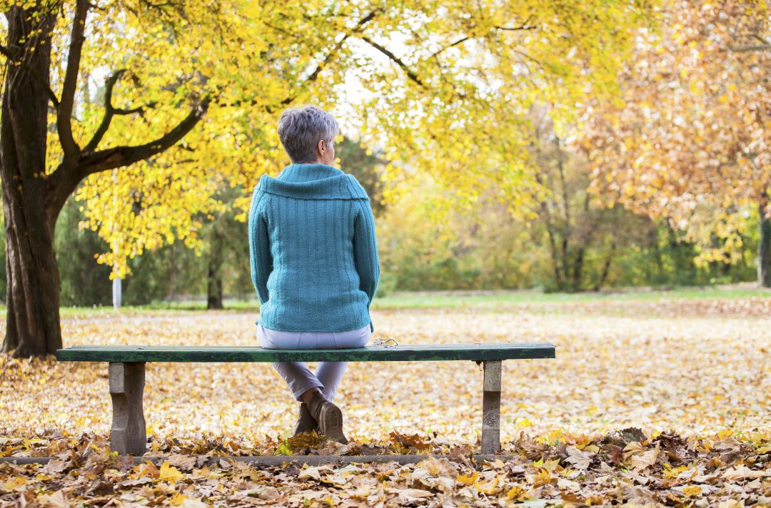 An older woman sitting on a bench in the park