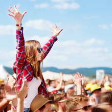 Woman at a festival sitting on someone's shoulders waving her hands in the air
